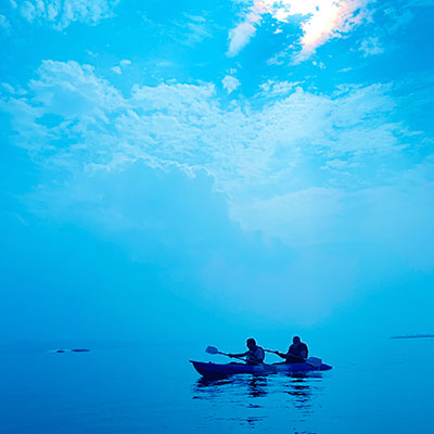 Two people kayaking under blue sky with sun shining